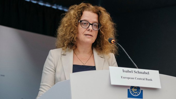 Woman with curly hair and glasses speaking at a podium with a nameplate reading 'Isabel Schnabel, European Central Bank' featuring the ECB euro logo.