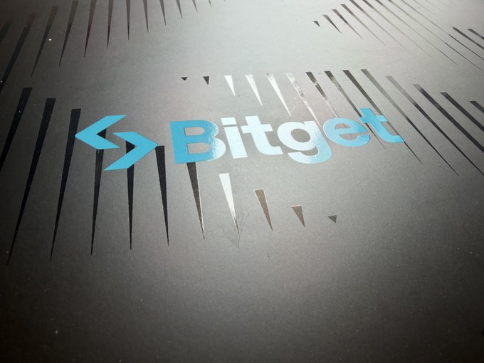 A blue Bitget logo on a black textured surface.