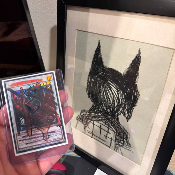 A hand holds a Yu-Gi-Oh! trading card in front of a framed sketch of an anime-style character with spiky hair.