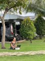 A person sitting on the grass in front of a building with a large mural, relaxing in a garden setting.