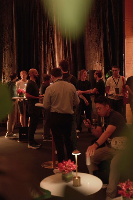 Guests gather and converse around small tables with glowing lamps and floral centerpieces in a dimly lit lounge setting, with some attendees checking their phones and others networking closely together.

The image reflects the post's description of a packed, well-attended event with great conversations, capturing the social atmosphere of the ether.fi Lounge where attendees engaged with sponsors like @Optimism, @ethena, @raincards, @plumenetwork, and @moonpay.