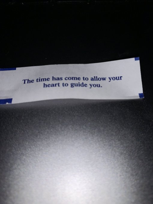 A fortune cookie slip on a dark surface reading 'The time has come to allow your heart to guide you.'
