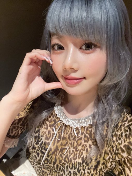 A close-up selfie of a woman with gray hair, wearing a leopard print top with a lace collar and drawstring detail, posing with her hand near her face.