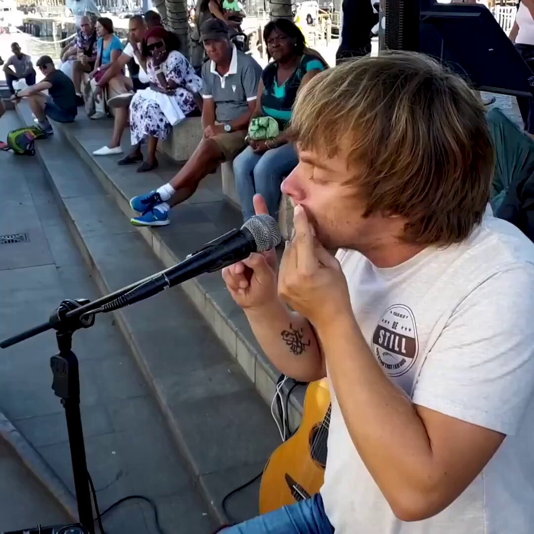 iced coffee and a microphone are set up on a stage, with people seated nearby and a backdrop of trees.