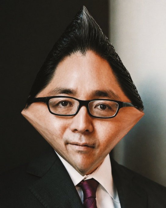 A man in a black suit, white shirt, and purple tie wears black-rimmed glasses, with his hair styled in an exaggerated tall point and his face digitally altered into a wide diamond shape.