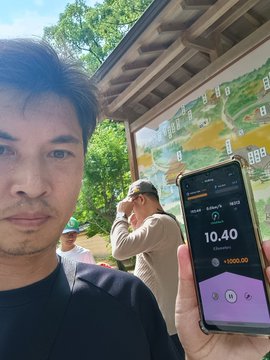 A man takes a selfie in front of a map near Kinkaku-ji (the Golden Pavilion) in Kyoto, holding up his phone showing the STEPN app with a current pace of 10.40 and +13000.00 earnings, while other tourists look at the map behind him. The image matches the post's caption about arriving at Kinkaku-ji while tracking steps on STEPN, skipping the visit, and fearing he won't hit his 21km goal back home.