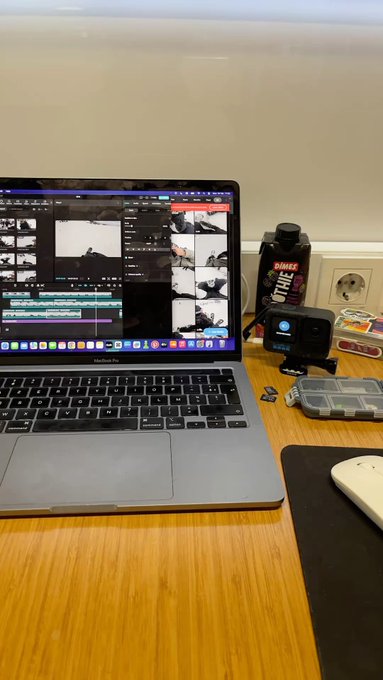 A workspace setup showing a MacBook Pro laptop running video editing software, with a water bottle and accessories on a wooden desk.