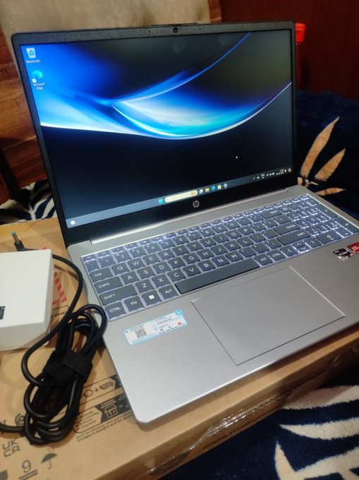 An HP laptop in a gray chassis sits on a cardboard box beside its power adapter, with its Windows desktop displayed on the screen. The image fits the $FOMO post by showcasing a new tech purchase as the "bullish opportunity" referenced in the message.