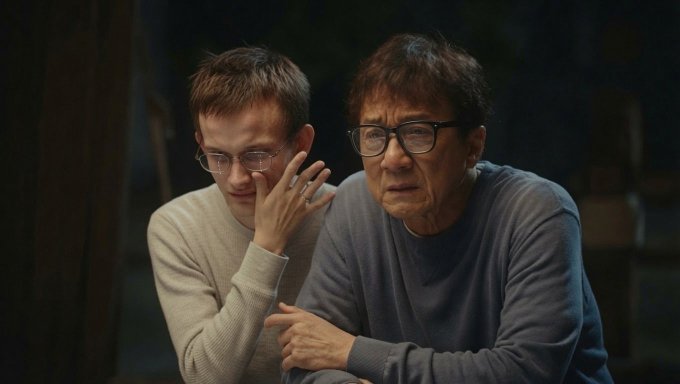 The image shows two people, a man wearing glasses and an older woman with short hair, sitting next to each other at a table. They are both looking at something off-camera, possibly engaged in conversation or observing something interesting. The background of the image is dark, which contrasts with the bright colors of their clothing. There is also text visible in the image that reads "Tom Lee losing - $8 billion after one year in Ethereum". This suggests that they might be discussing a recent news article about someone losing a significant amount of money through cryptocurrency trading or investing.