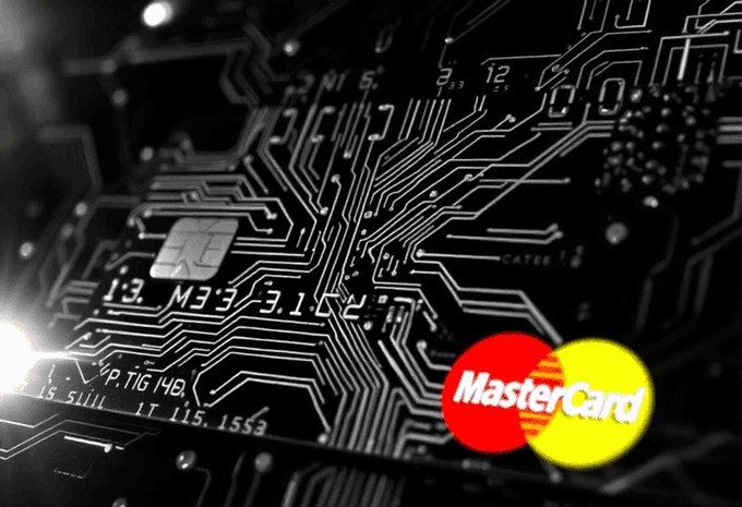 A close-up black and white image of a credit card's circuit board/chip pattern overlaid with the red and yellow MasterCard logo in the bottom right corner.
