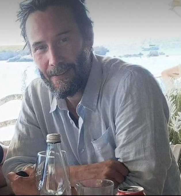A bearded man in a light button-up shirt sits at an outdoor table with bottles and glasses, smiling modestly at the camera. The serene seaside backdrop and his humble demeanor visually reinforce the post's message that XRP holders should remain grounded, grateful, and gracious after gaining wealth.