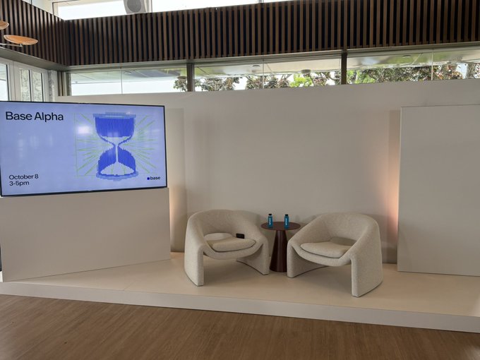 An empty interview stage with two chairs and a screen displaying 'Base Alpha, October 8, 3-5pm' with a blue hourglass graphic.