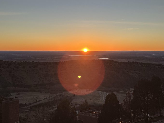 A serene sunrise illuminates a vast landscape of rolling hills and distant plains, with the bright sun hovering on the horizon and its reflection captured in a lens flare below.

The image of a peaceful dawn mirrors the post's theme of fresh starts and steady progress, visually reinforcing the message that small, consistent improvements—like waking up to greet the day—can lead to meaningful change.