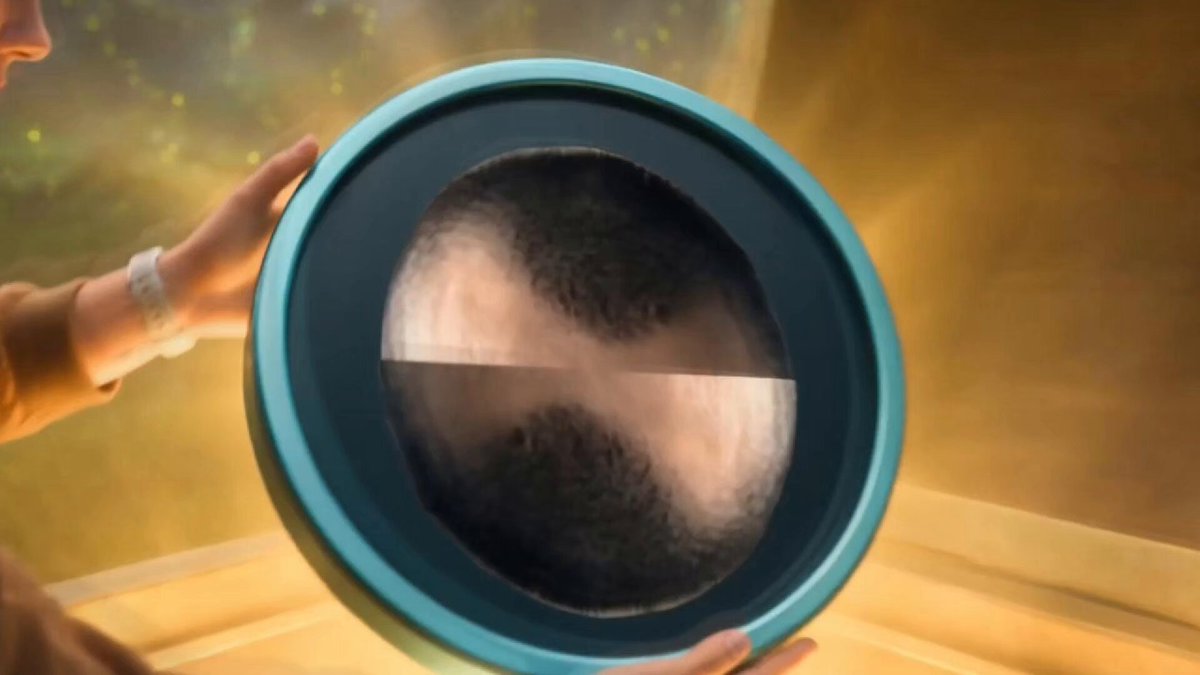 The image features a person holding up a round, blue-green plate with a black design on it. The plate has a unique design that resembles a globe or planet, which adds an interesting visual element to the scene. The background of the image is blurred, drawing attention to the plate and making it the focal point of the photo.