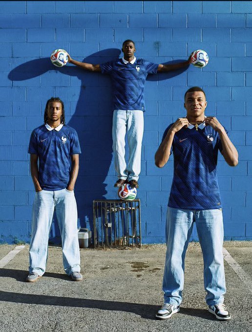 A photo of three young men in France national team soccer jerseys posing in front of a blue wall, with the middle man balancing on a soccer ball while holding two more.