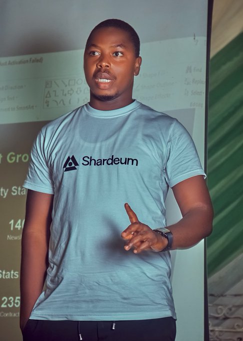 A young man wearing a light blue t-shirt featuring the "Shardeum" logo stands in front of a whiteboard, gesturing as he speaks—likely presenting insights on Web3 marketing strategies, aligning with the post's discussion on how Web3 companies approach their promotional efforts.