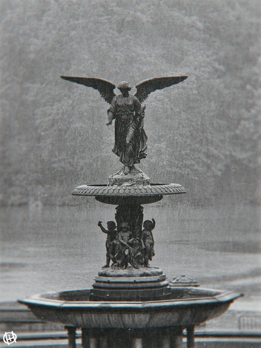 A vintage-toned photograph captures an ornate bronze fountain featuring a winged angel statue at the top and small cherub figures at the base, set against a stone wall.