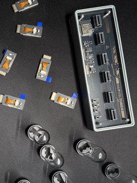 A photo of a 4K@120Hz USB hub device alongside its component parts, including small circuit boards and suction cups, laid out on a dark surface.