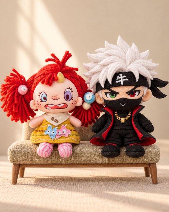 Two crocheted amigurumi plush dolls sit on a small beige couch: a red-haired character in a yellow dress on the left, and a white-haired ninja-like character in a black outfit with a red-lined cape and a headband marked with a cross-shaped symbol on the right.