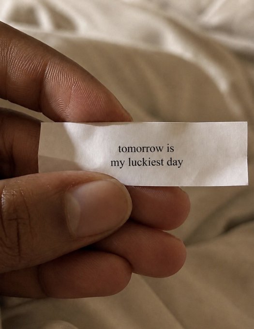 A close-up of fingers holding a fortune slip that reads "tomorrow is my luckiest day," fitting the post's "Claim it" message as a manifestation of optimism about what's to come.
