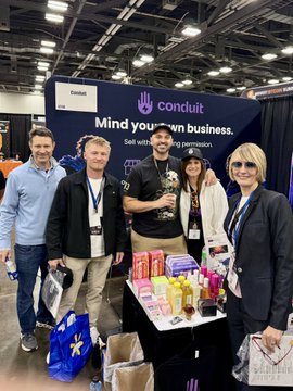 Five people pose in front of a 'conduit' booth that reads 'Mind your own business. Sell with the permission to grow.' at what appears to be a trade show or conference.