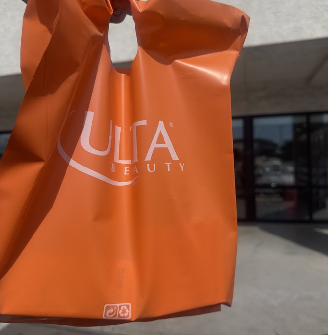 A person holds an orange Ulta Beauty shopping bag in front of what appears to be the storefront, with the brand's white "ULTA BEAUTY" logo clearly visible. The bag illustrates the post's message of purchasing beauty/skincare products—likely to stay moisturized—after a desert move, made possible with a gift card via DashPay.