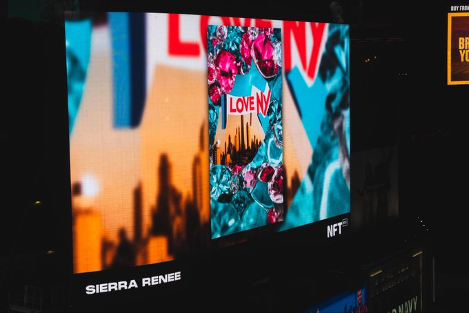A Times Square billboard at night displaying an NFT artwork by 'SIERRA RENEE' featuring a 'I LOVE NY' theme with floral elements and the NFT logo.