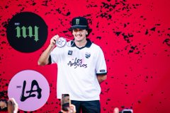 A person wearing a top hat and a white 'Angels' baseball jersey holds up a small medallion against a red splatter background with the 'LA' Angels logo, under a 'MY' circular badge.