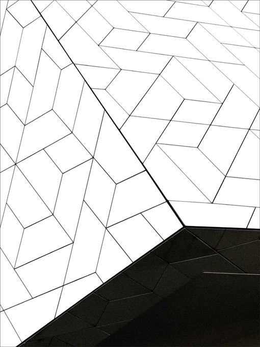 An abstract geometric pattern featuring angular shapes in white, gray, and black tones, creating a faceted, architectural design.