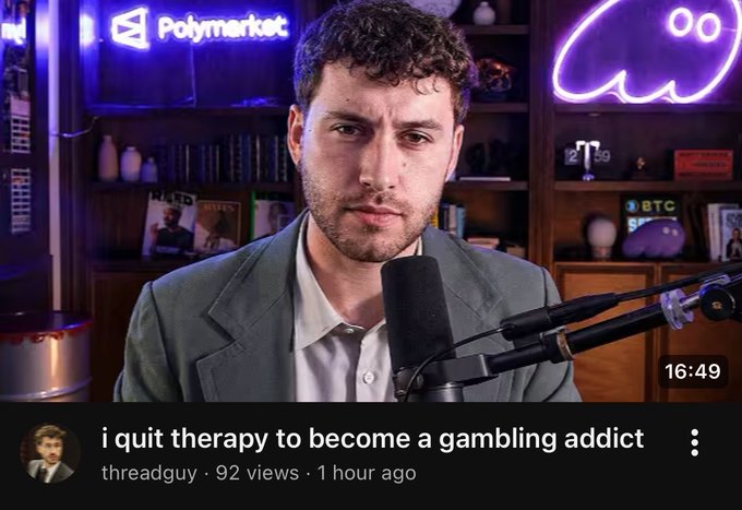 A man in a gray suit speaks into a microphone in front of a shelf with a glowing "Polymarket" sign and ghost neon light, with the video titled "i quit therapy to become a gambling addict" by threadguy, showing 92 views from 1 hour ago and a timestamp of 16:49.