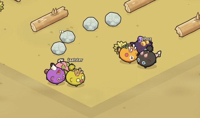Two teams of cute, colorful round creatures with names "jaatster" (purple, pink, green) and "jihoz" (orange, black, purple) face off on a sandy arena with spiked logs and stone obstacles, evoking a playful yet tense competitive feeling.