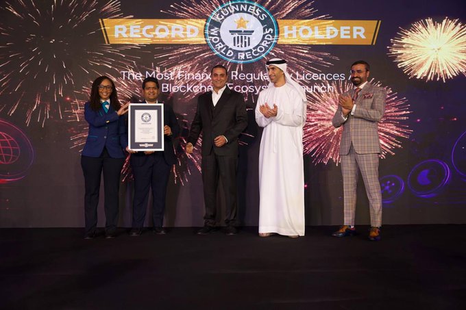 Five people stand on stage holding a Guinness World Records certificate at a "Record Holder" ceremony, with the backdrop reading "The Most Primary Regulated Licences / Blockchain Ecosystem Launch," celebrating Blockmaze's achievement of launching 24,000+ tokenized stocks through their Dealing platform as a global market infrastructure milestone.