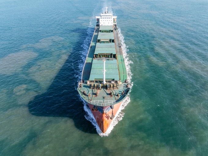 An aerial view of a large cargo ship sailing through open waters, with its green cargo hatches and white superstructure clearly visible from above, serving as a visual representation of the shipping industry context behind EthraShip and SeaVerity's maritime analytics platform metrics.