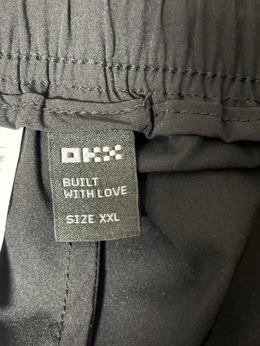 A close-up of a clothing label reading 'OKX BUILT WITH LOVE SIZE XXL' attached to a black garment.
