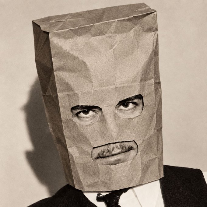 A sepia-toned photo shows a person wearing a brown paper bag over their head with eye and mouth holes cut out, dressed in a suit and tie. The image relates to the post by symbolizing anonymous accumulation of the $ZCAT token, suggesting the user is quietly building a position without revealing their identity.