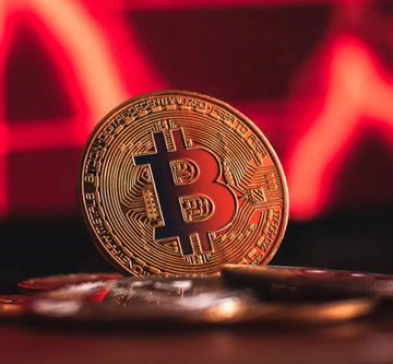 A physical Bitcoin token with the iconic "B" logo sits in the foreground against a blurred red downward-trending chart, visually reinforcing the WSX News post's prediction of Bitcoin ($BTC) potentially dropping to $59,000 as traders price in a deeper pullback on Kalshi.