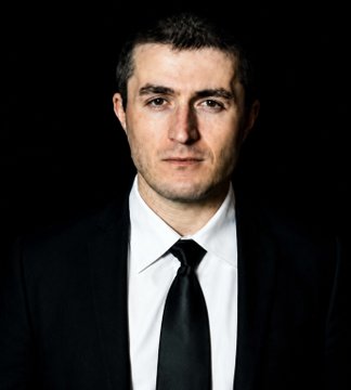 A formal portrait of a man in a dark suit and black tie against a black background, with a serious expression. The image appears to accompany a post featuring a quote attributed to Lex Fridman advocating that Satoshi Nakamoto should receive the Nobel Prize.