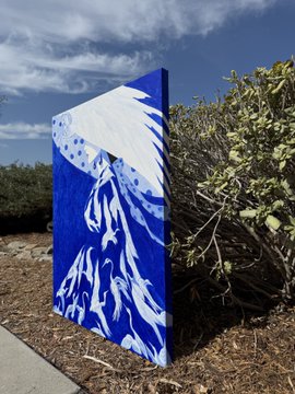 A large, finished blue and white abstract painting rests outdoors against shrubs, featuring bold white brushstrokes that contrast against the deep blue canvas, marking the completion of the artwork the artist has just finished.