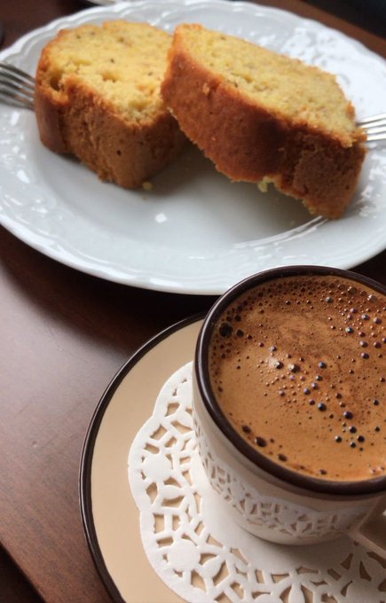 Two slices of yellow pound cake on a white decorative plate next to a cup of frothy coffee served on a lacy doily.