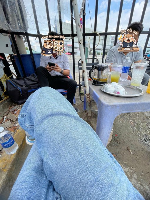 A casual outdoor scene shows people sitting at a small plastic table with drinks, while someone's legs in blue jeans are visible in the foreground.