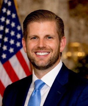 The image shows a smiling man in a dark suit and blue tie posing in front of an American flag, which aligns with the post referencing Eric Trump's bullish comment on gold profits rotating into Bitcoin. His appearance in a formal, patriotic setting reinforces his role as a public commentator on financial markets.