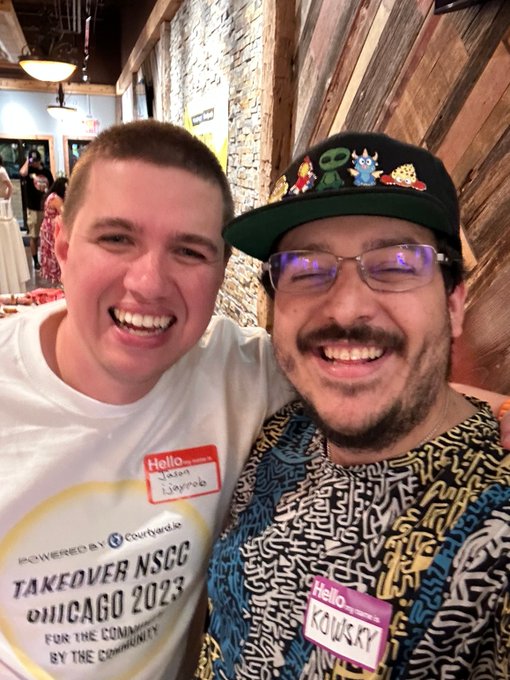 Two smiling men pose together at an event, wearing name tags that read "Hello my name is 1Bryanb" and "Hello my name is KROWSKY," with one wearing a shirt that says "TAKEOVER NSCC CHICAGO 2023".