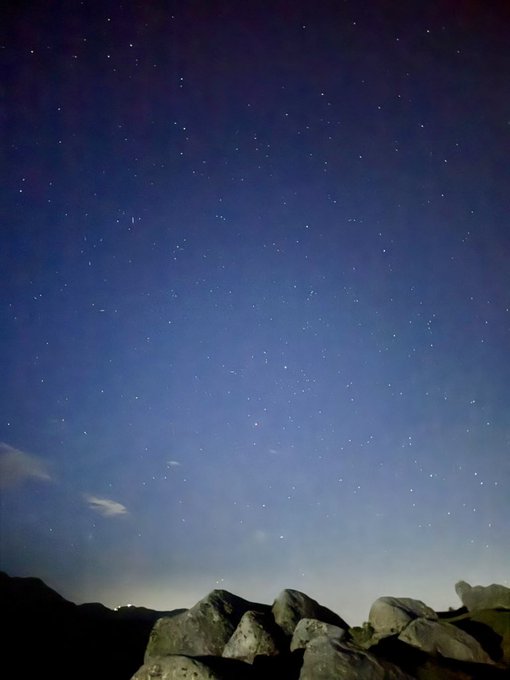 The image shows a night sky filled with stars against a dark blue backdrop. The scene appears to be taken from a rocky area, possibly at the top of a mountain or near a cliff. In the bottom right corner of the photo, there is text that reads "Good morning champions @NomismaNetwork is taking a more adaptive approach to protocol coordination, improving how liquidity and incentives move across the ecosystem as network conditions change over time @River4fun is refining its reward model with smarter participation".