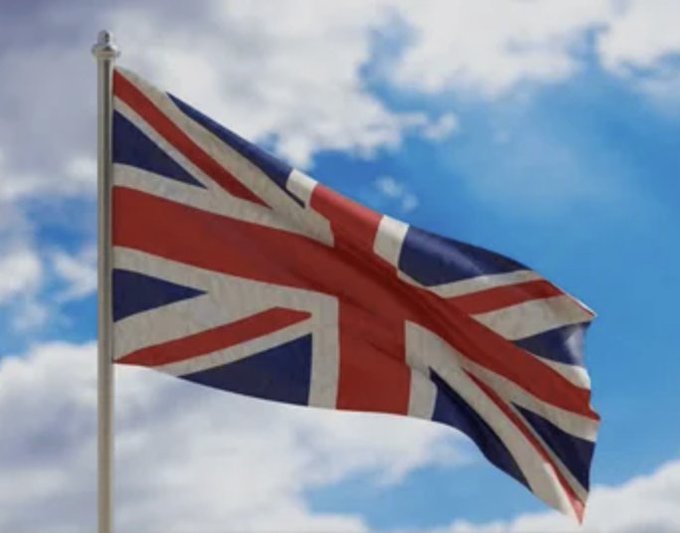The Union Jack flag waves against a blue sky with scattered clouds. The image visually represents the United Kingdom, aligning with the post about UK Labour MPs pushing for a permanent ban on crypto political donations.