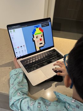 A child uses a MacBook to create pixelated "CryptoPunk"-style character art, having generated 35 punks in under an hour, and is asking their parent about NFT ownership of the numbered digital assets they created.