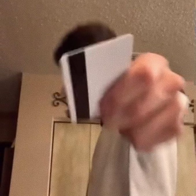 A blurry image of a person's hand holding a white card near a dark circular hole above a decorative doorway.