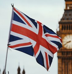 The Union Jack flag of the United Kingdom waves in the wind with the iconic Big Ben clock tower visible in the background.