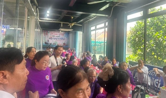 A crowded meeting space in Bắc Ninh, Vietnam, where attendees — many wearing matching purple shirts — are gathered for a Global PI GCV Peace Alliance training event, as indicated by the banner reading "NGÀY HỘI..." in the background. The scene reflects the educational and community-building focus of the gathering, with participants seated closely together listening attentively.