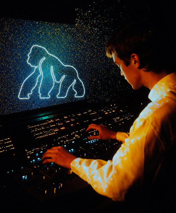 A stylized photograph of a young person operating a large sound mixing console illuminated by numerous small lights, with a projection of a glowing gorilla outline on a dark background screen.