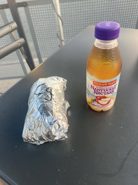 A foil-wrapped Chipotle burrito sits on a dark table next to a bottle of Nantucket Nectar juice, serving as visual proof of a Chipotle dinner purchased with Zcash (ZEC) cryptocurrency via the Flexa network through the SPEDN app.